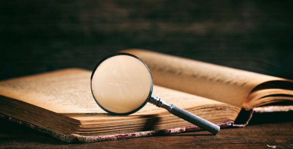 Vintage book and magnifying glass on wooden background