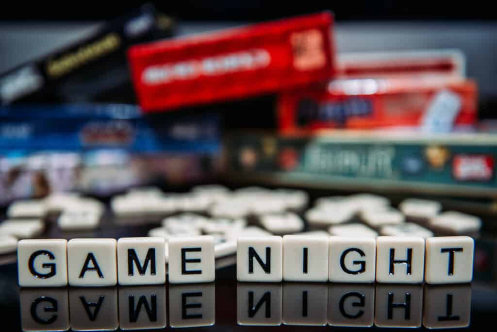 Game Night spelled out in letter tiles on black background with boardgames in the background
