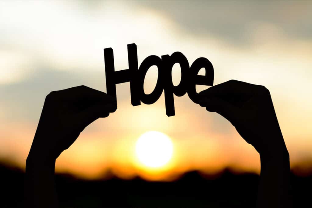 Silhouette hands holding the word hope. Background Sunset.