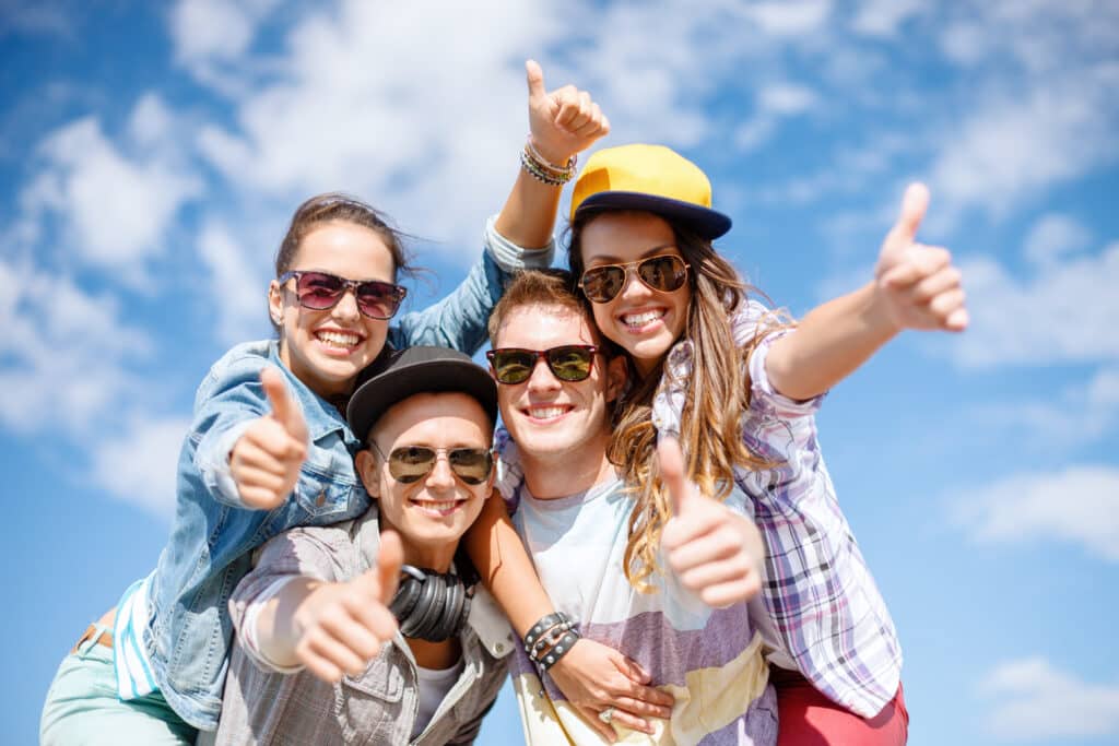 summer holidays and teenage concept - group of smiling teenagers in sunglasses hanging outside and showing thumbs up